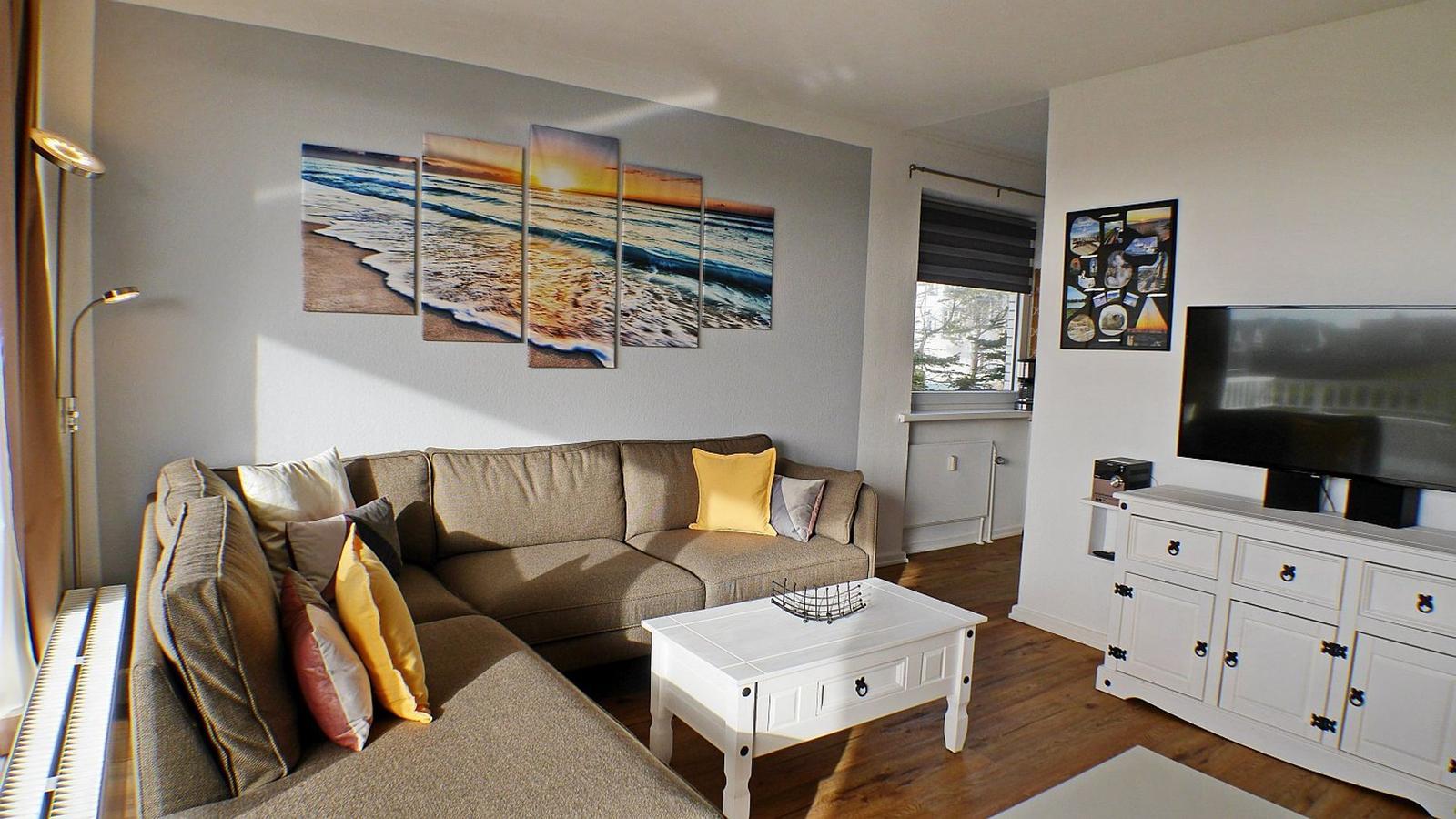 Wohnzimmer mit Sofa, Couchtisch und Fernseher. Wandbild zeigt Strand.