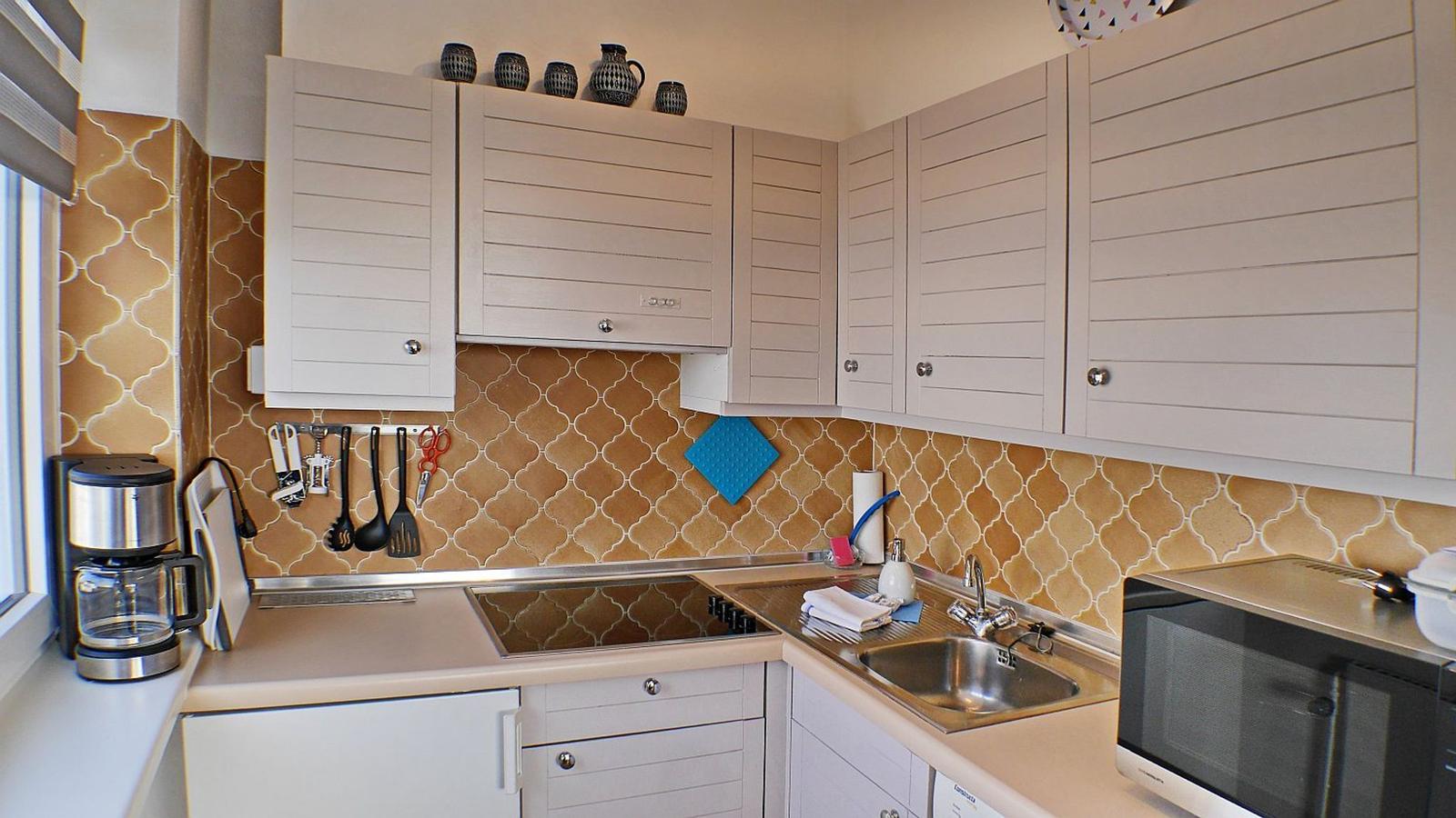 Küche mit weißen Schränken, Mosaikwand und Edelstahlspüle.