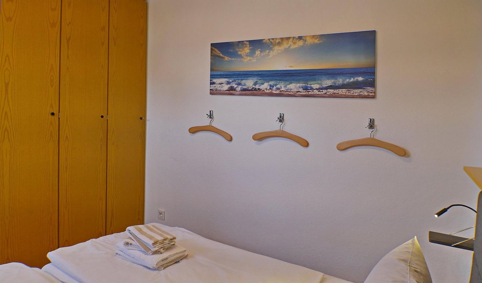 Schlafzimmer mit Bett, Kleiderhaken und Wandbild mit Strandmotiv.