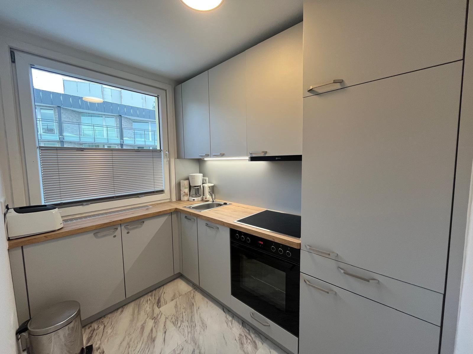 Kitchen with light cabinets, wooden countertop, and window with blinds.