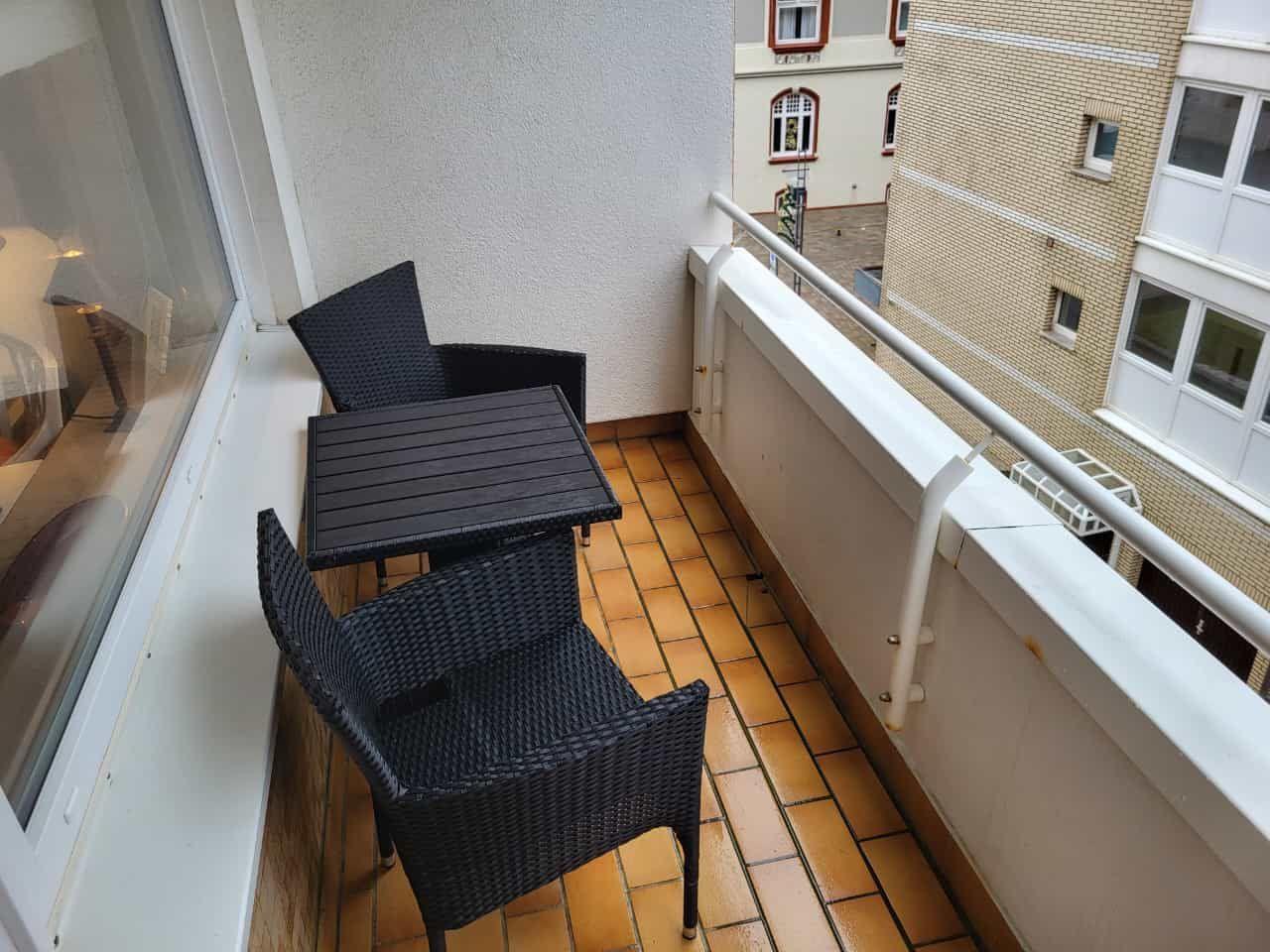 Balcony with table and two chairs, tiled floor and railing.