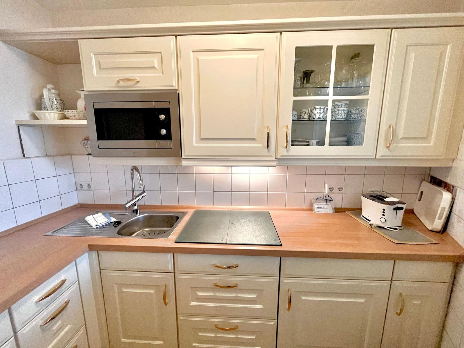 Kitchen with white cabinets, wooden countertop, sink, and microwave.