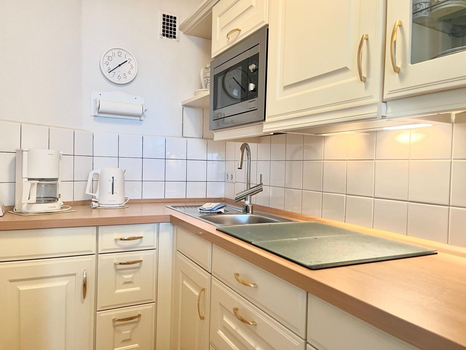 Kitchen with white cabinets, wooden countertop, sink, and microwave.