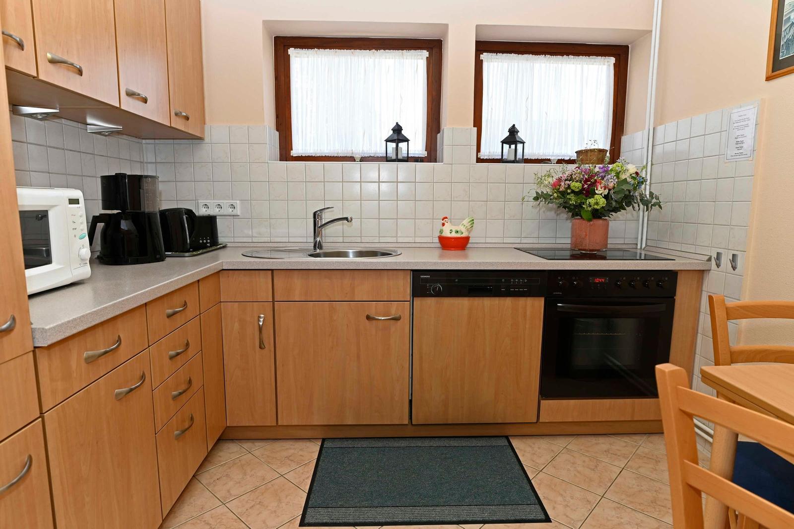 Kitchen with wooden cabinets, sink, stove, and microwave. Two windows with white curtains.