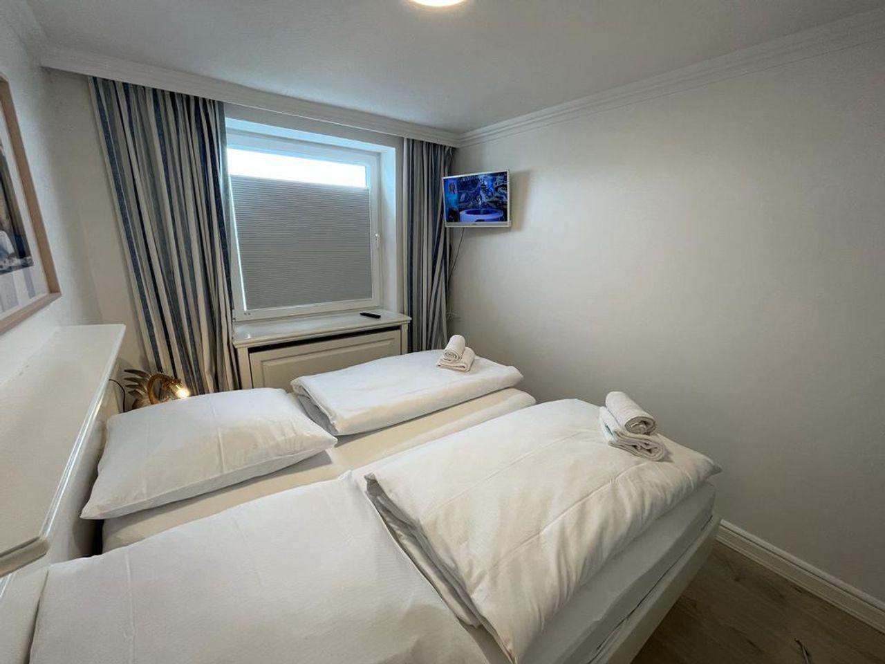 Room with two beds, window with blinds, and wall-mounted TV.