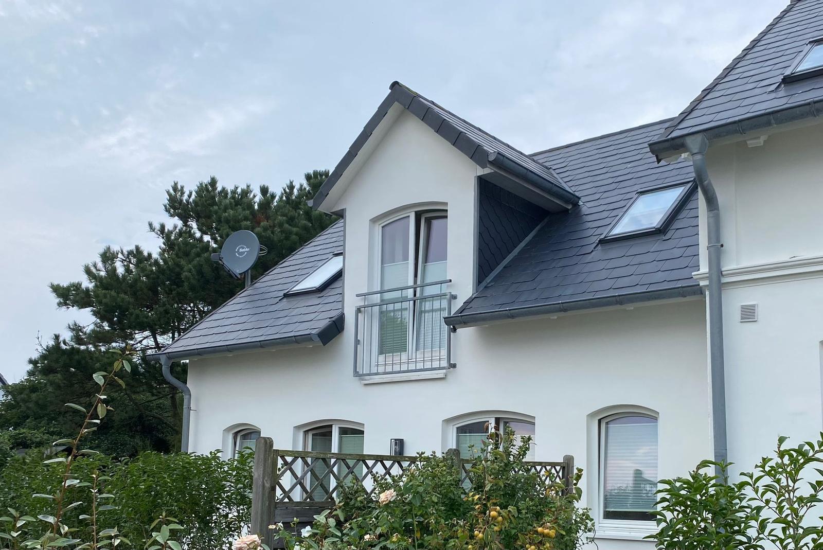 Wohnhaus mit Balkon, Dachfenstern und Satellitenantenne. Umgeben von Grünflächen.
