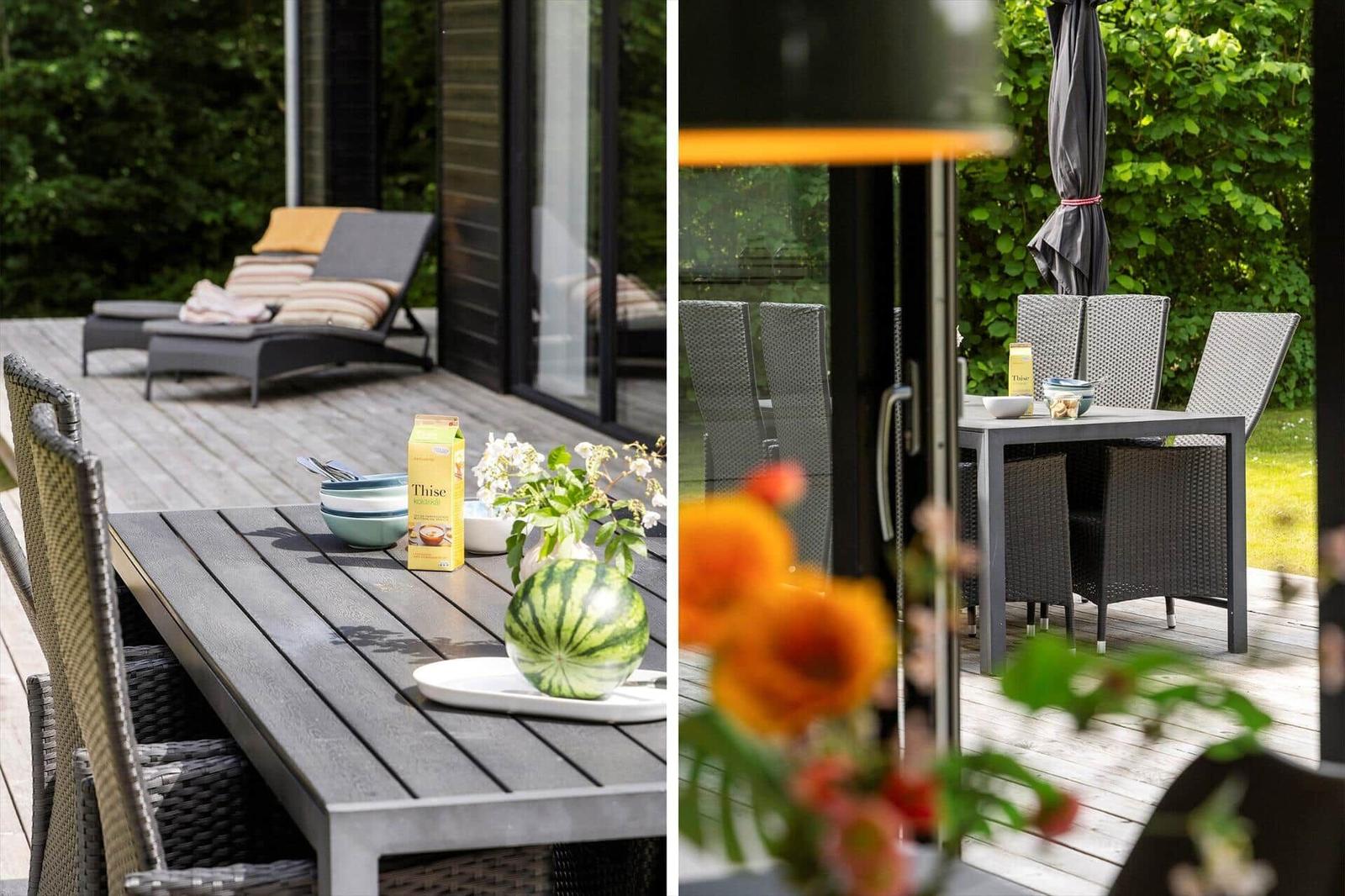 Terrasse mit Esstisch, Liegestühlen und Wassermelone. Hintergrund: grüne Vegetation und Glasfassade.