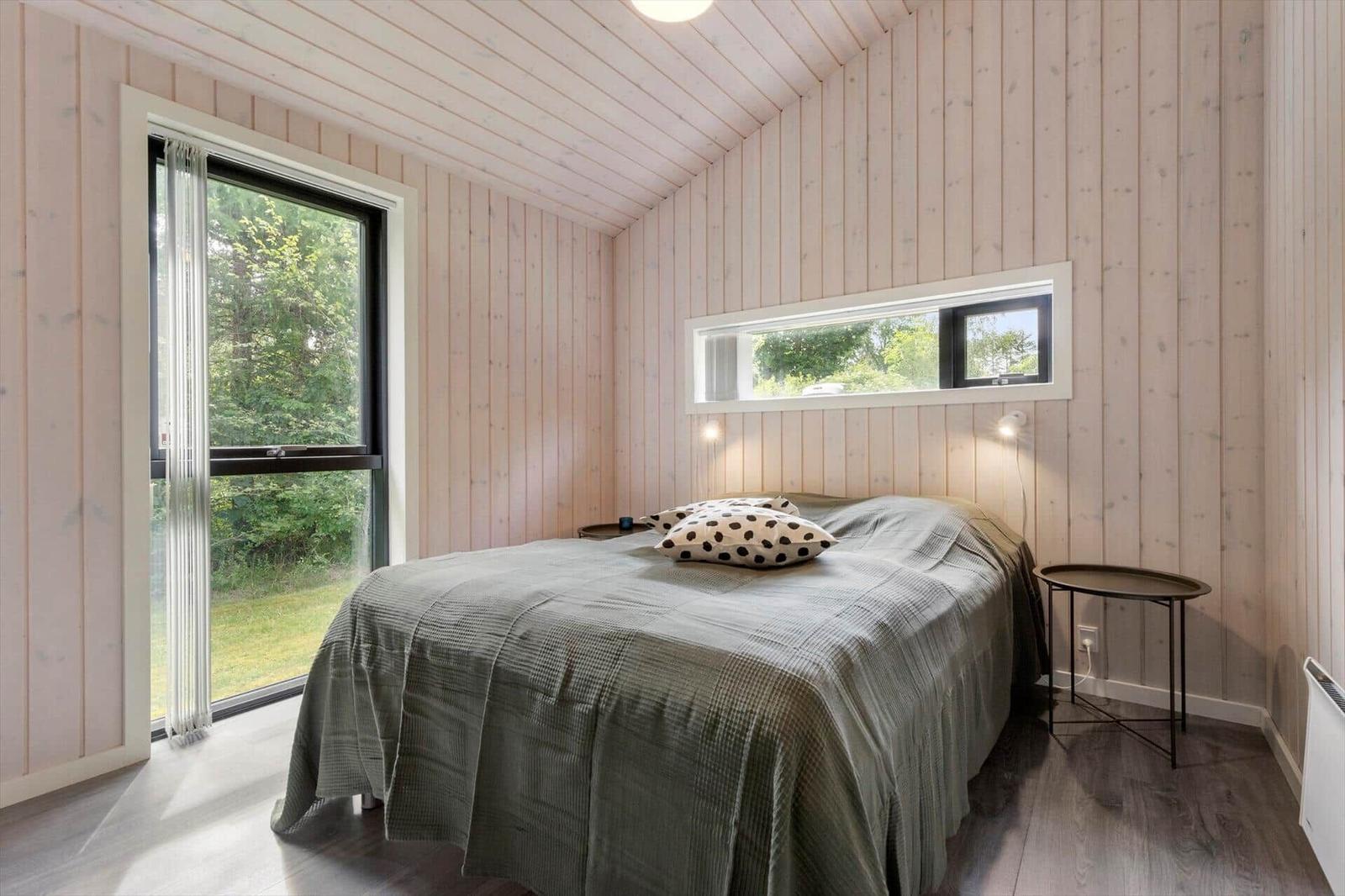 Schlafzimmer mit Holzwand, Bett, Fenster und Tisch.