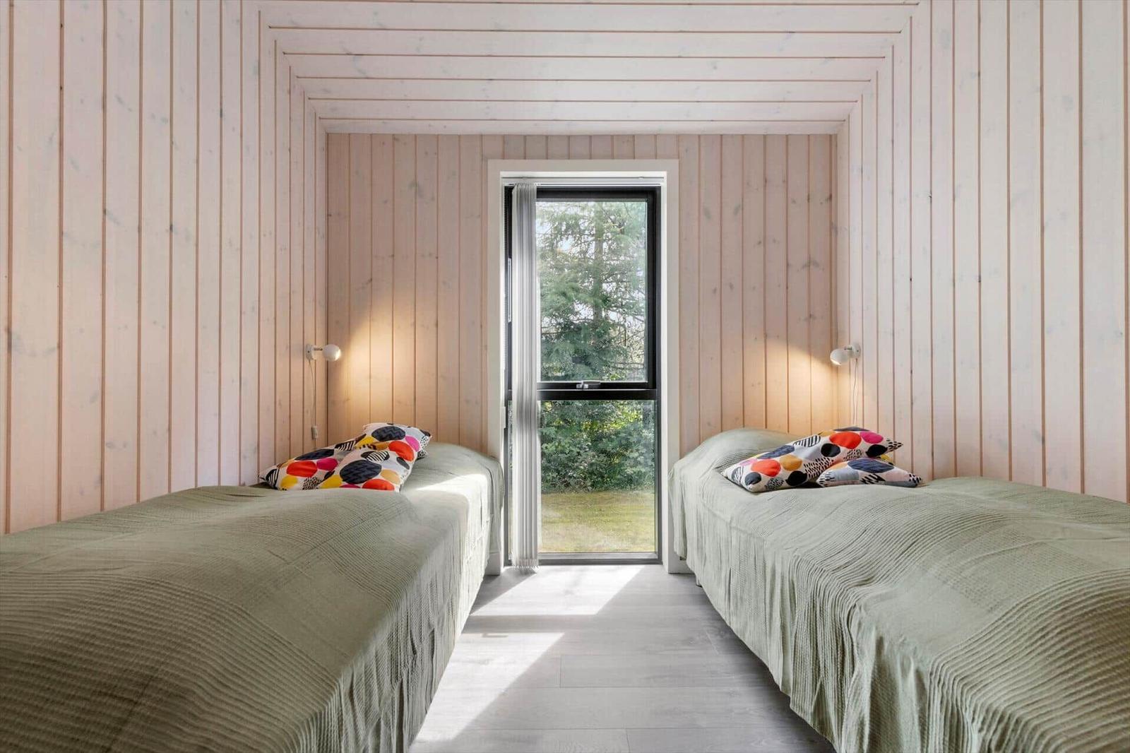 Zwei Betten mit bunten Kissen stehen in einem Raum mit Holzwandverkleidung und einem Fenster.