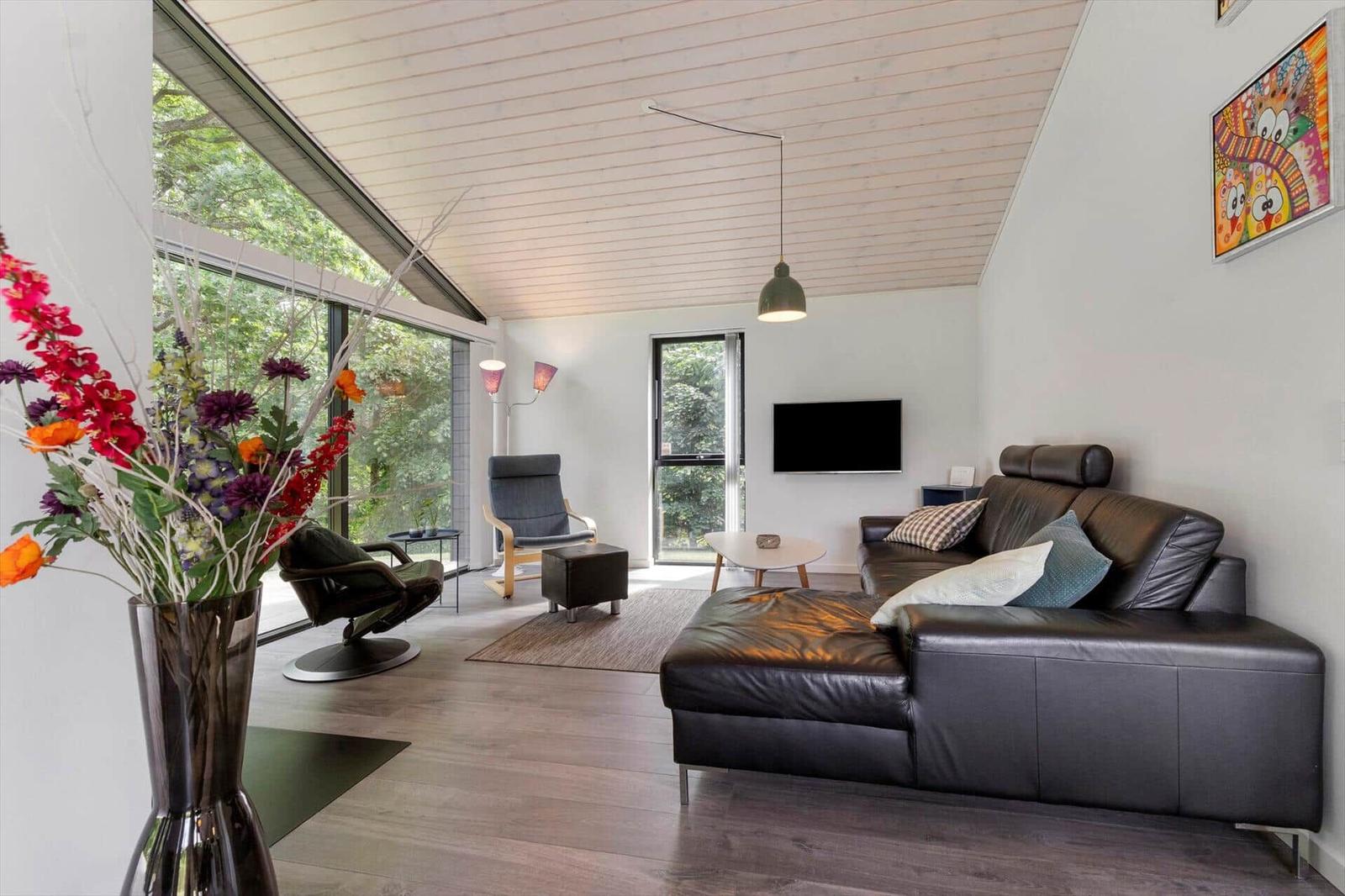 Wohnzimmer mit Ledersofa, großen Fenstern und Holzboden.