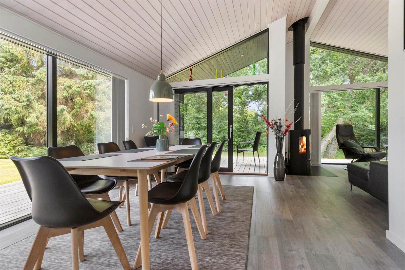 Essbereich mit Tisch, Stühlen und Blick auf Garten. Kamin und Sitzgelegenheit im Hintergrund.