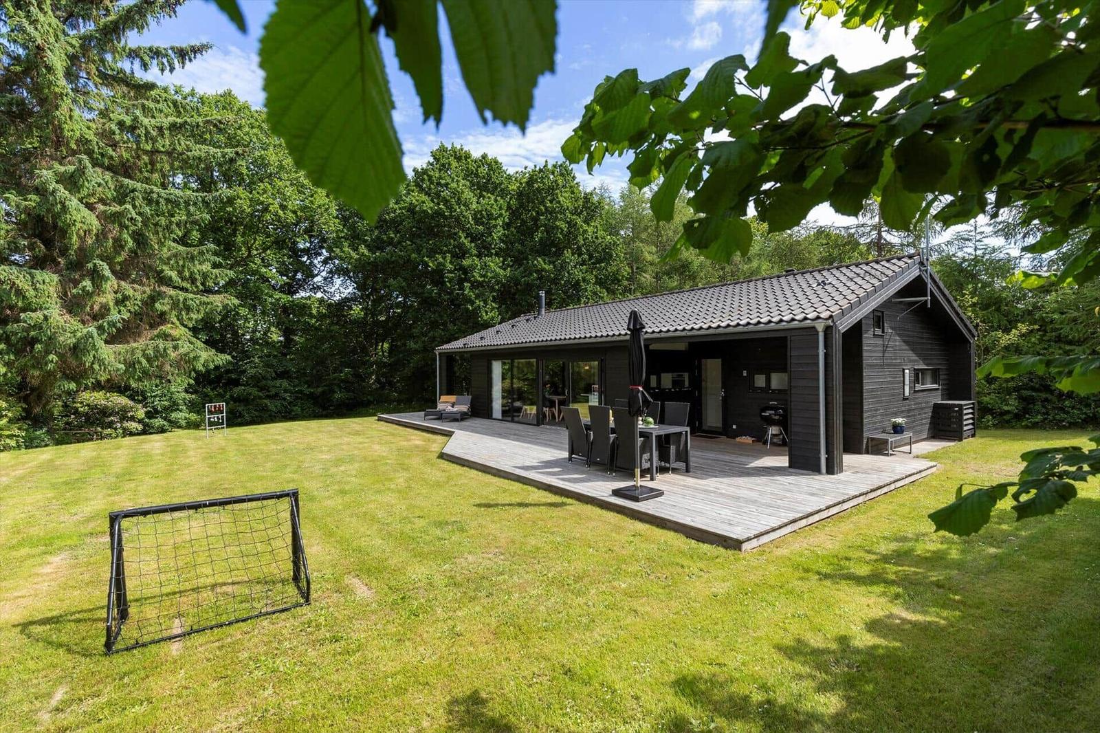Ein modernes Haus mit Terrasse, Grill und Fußballtor auf grünem Rasen.