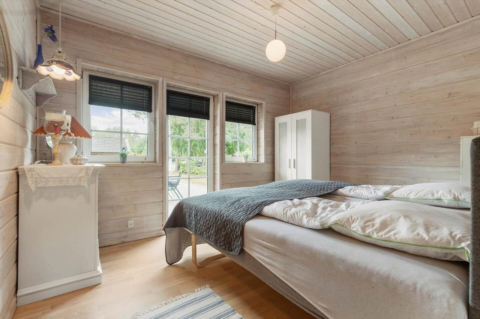 Schlafzimmer mit Holzwand, Bett, Kleiderschrank und Fenstern.