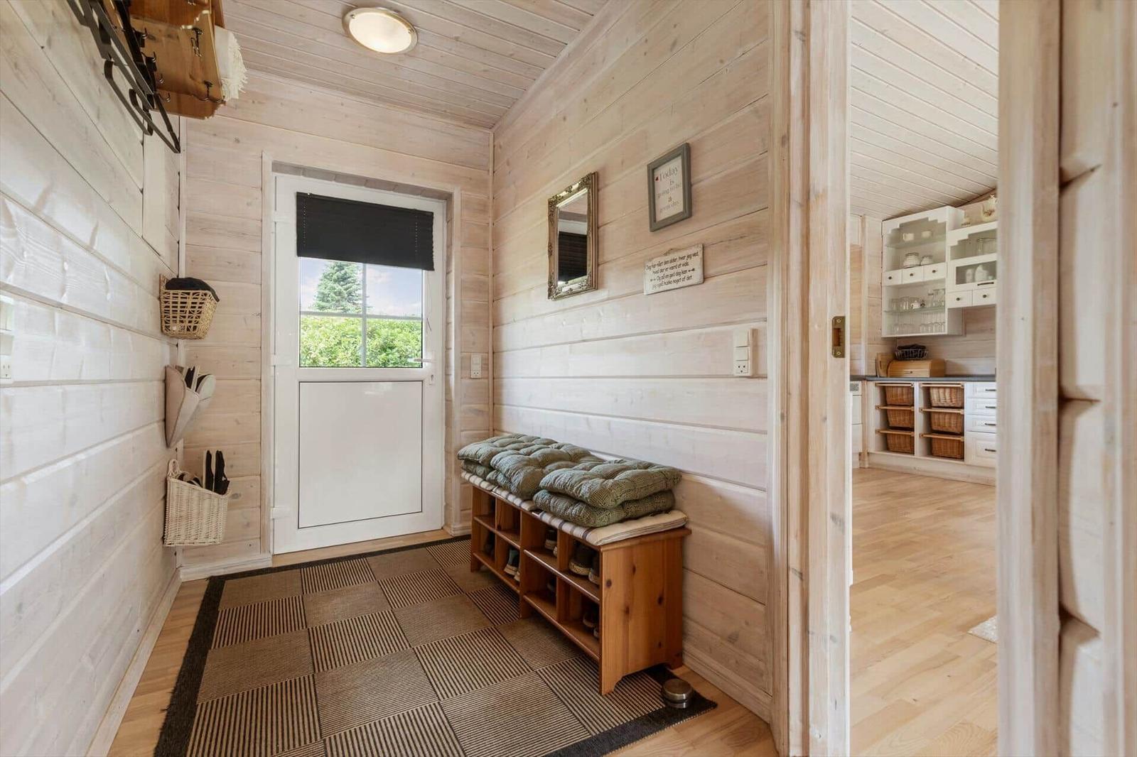 Eingangsbereich mit Holzwand, Sitzbank und Blick in die Küche.