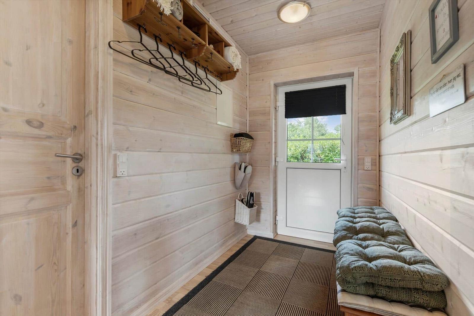 Eingangsbereich mit Holzwand, Garderobe und Sitzbank vor der Tür.
