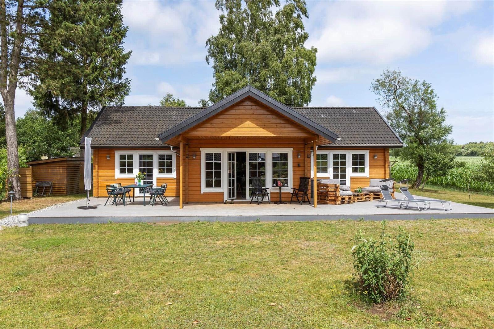 Holzhäuschen mit Terrasse, Garten und Liegen. Fenster und Türen sind weiß.