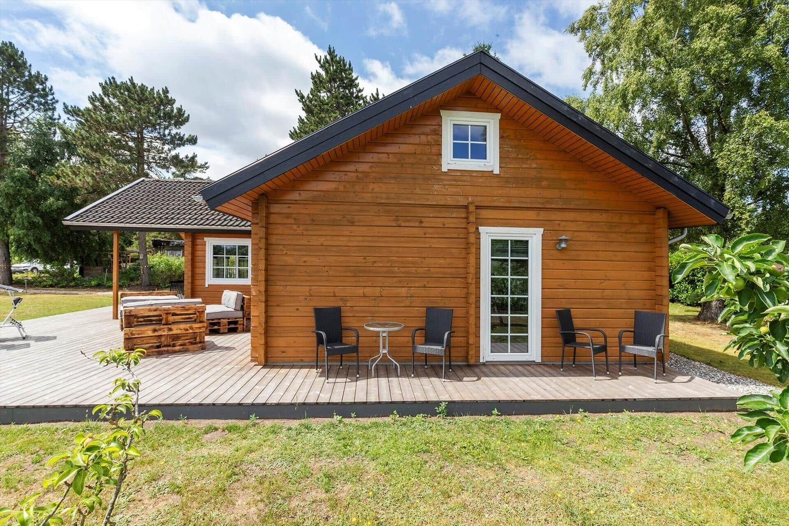 Holzhütte mit Terrasse, Garten und Sitzgelegenheiten. Fenster und Tür sind weiß.