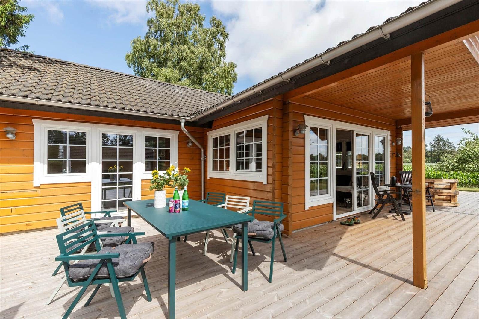 Holzhaus mit überdachter Terrasse, Tisch und Stühle. Blick auf Garten und Himmel.