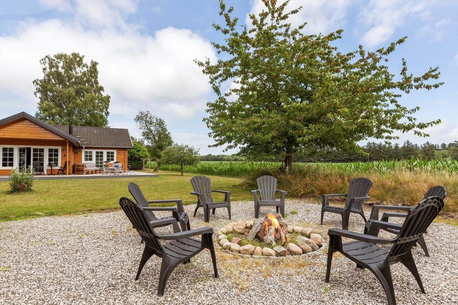 Feuerplatz mit Sitzgelegenheiten im Freien vor einem Holzhaus mit Garten.