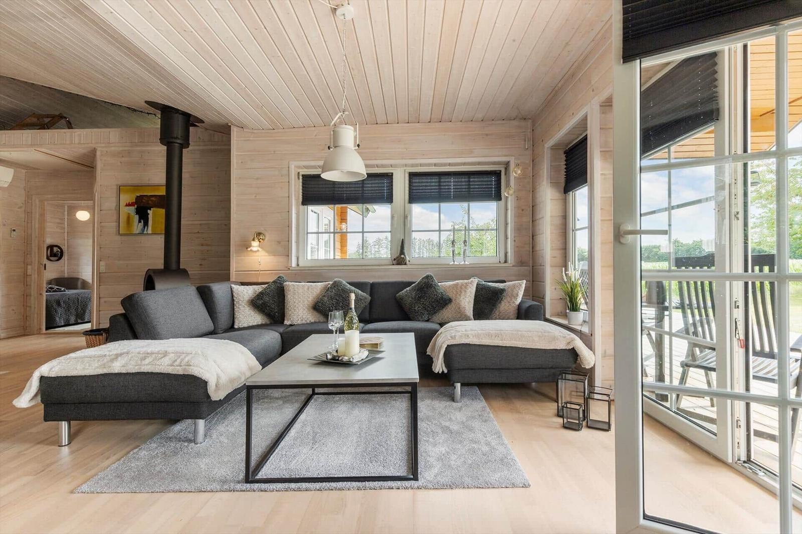 Ein Wohnzimmer mit grauem Sofa, Holzwänden und einer Terrasse.