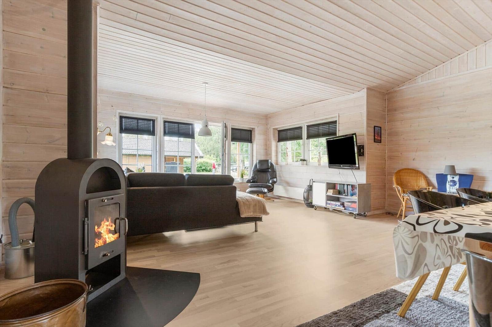 Wohnraum mit Kamin, Sofa, Fernseher und Essbereich. Holzwände und -boden.