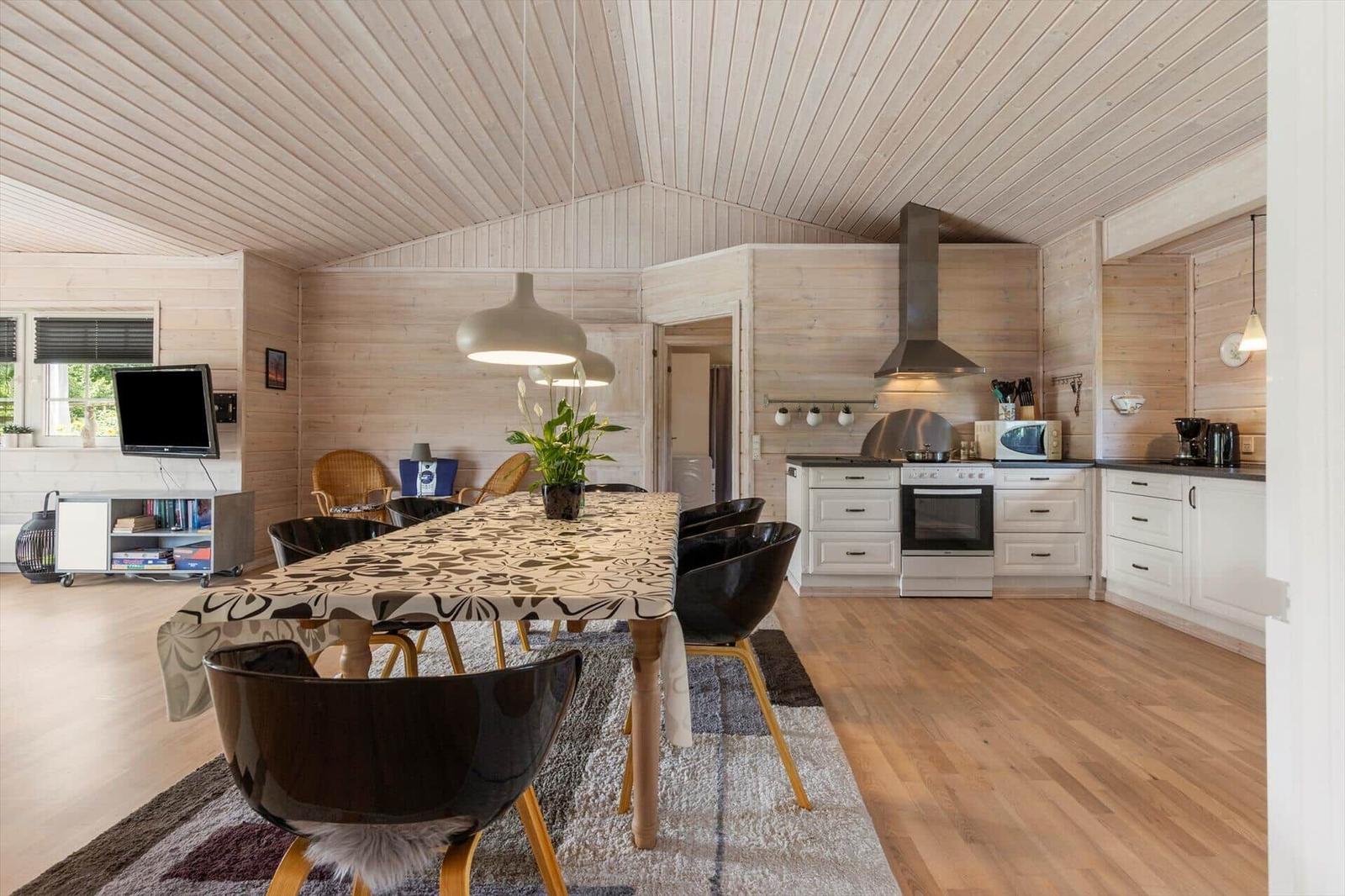 Küche und Essbereich mit Holzwand und -boden. Esstisch mit Stühlen und TV.
