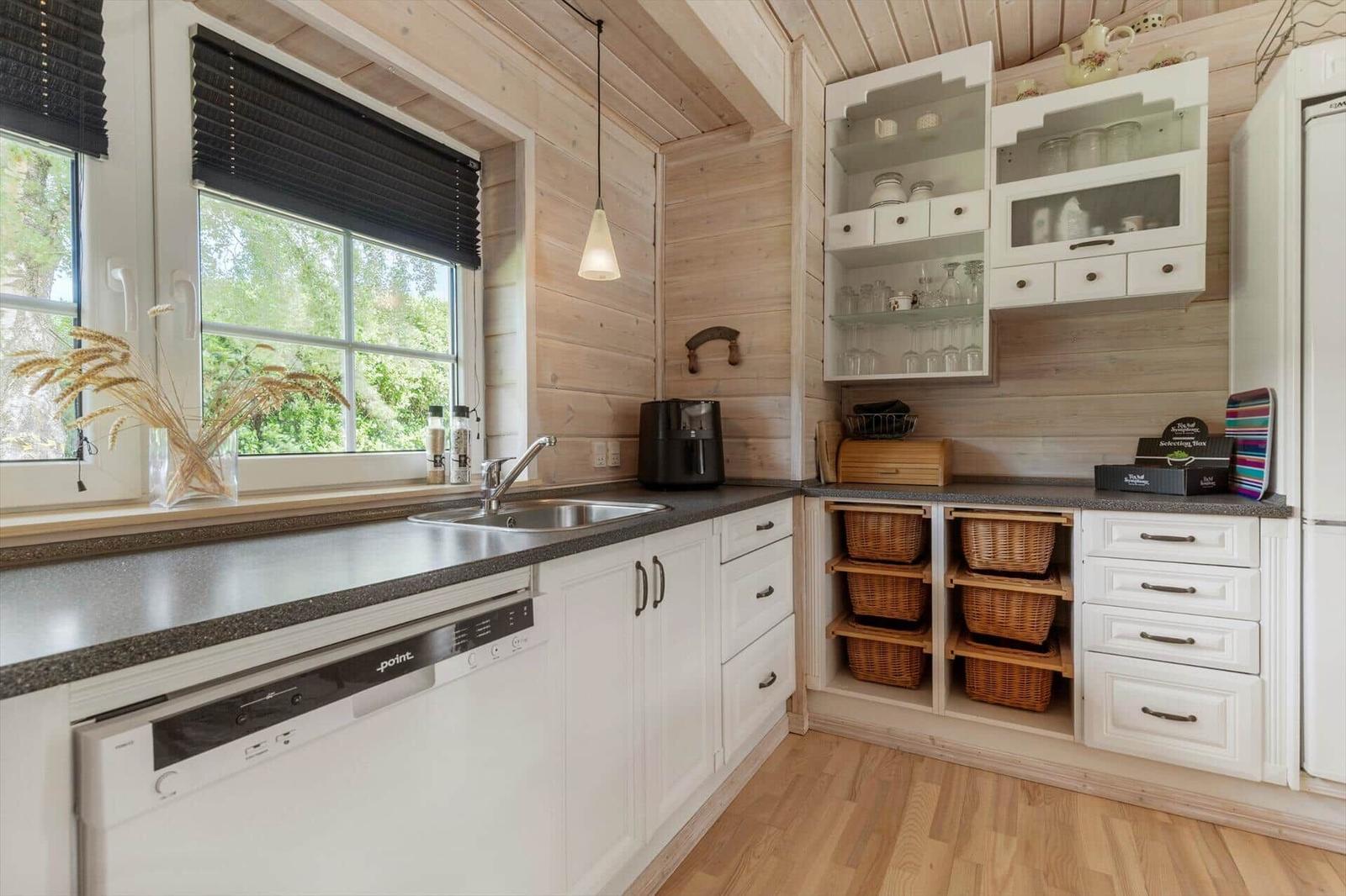 Küche mit Holzwänden, weißen Schränken und Fenster mit Blick auf Grün.