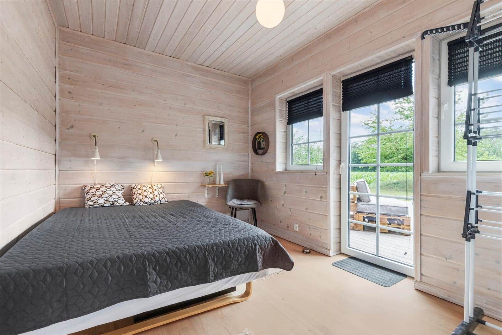 Schlafzimmer mit Bett, Fenstern und Balkontür. Holzwände und Boden.