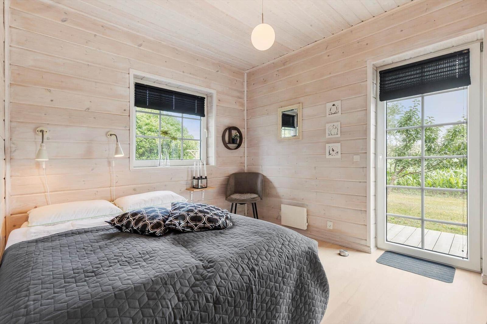 Schlafzimmer mit Holzwand, Bett, Fenster und Glastür zum Garten.