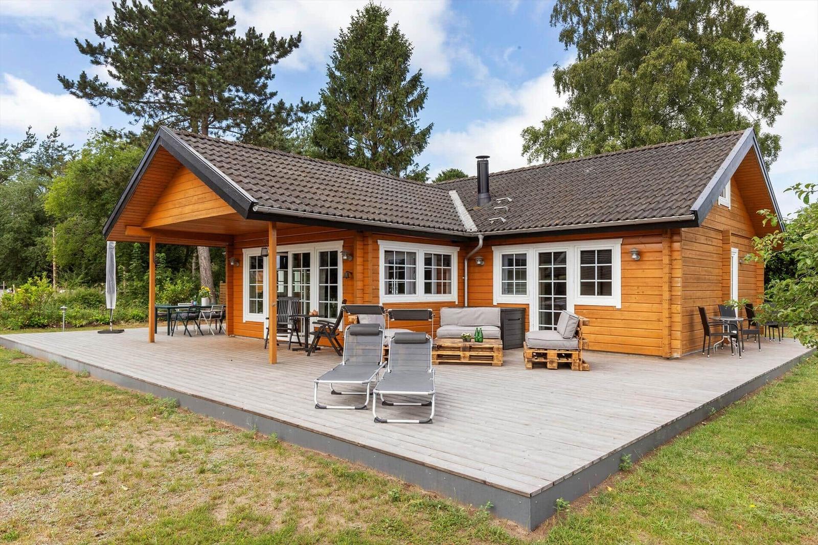Holzhaus mit Terrasse, Liegestühlen und Garten. Fenster und Türen sind weiß.