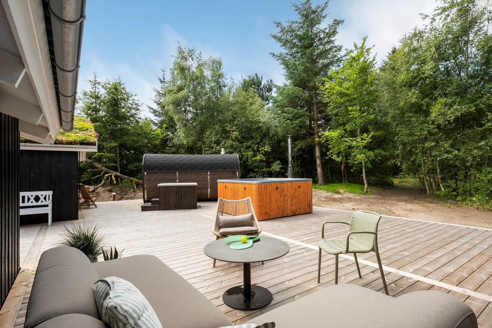 Terrasse mit Sitzgelegenheiten, Whirlpool und Holzsauna im Wald.