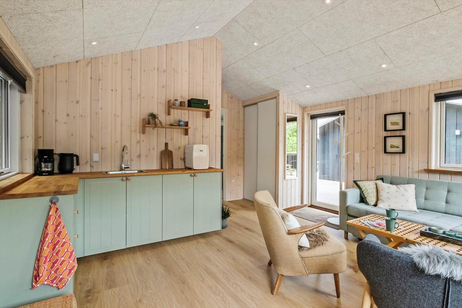 Küche mit Holzwand und hellblauen Schränken. Wohnbereich mit Sofa und Sessel.
