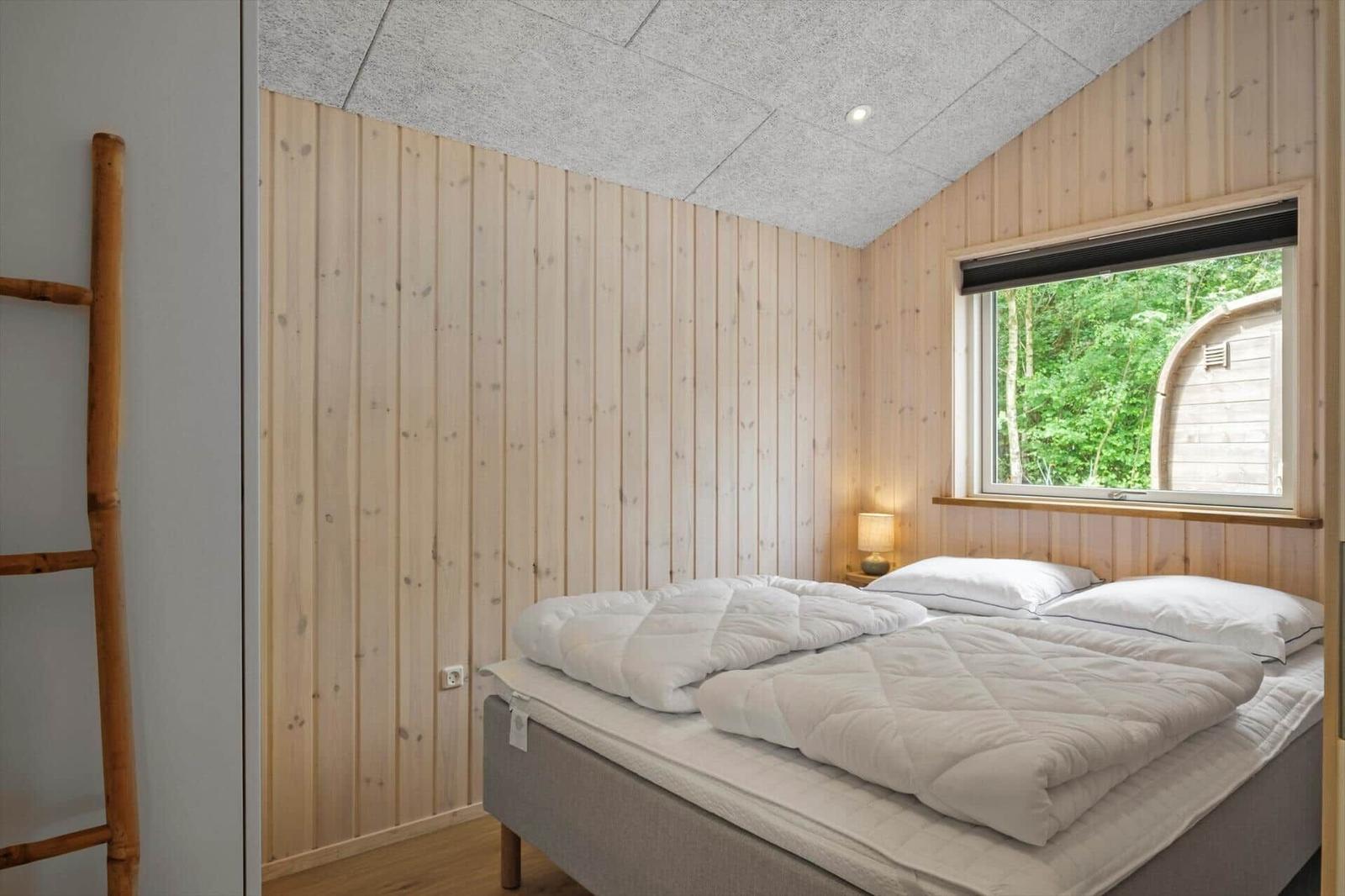 Schlafzimmer mit Holzwand, Bett und Fenster zum Wald