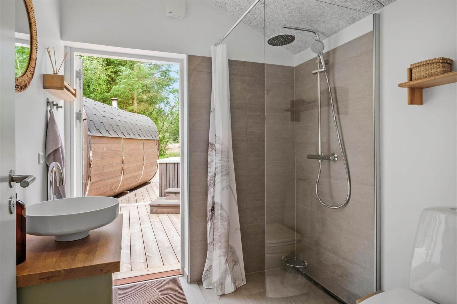 Badezimmer mit Dusche, Waschbecken und Blick auf Holzsauna.