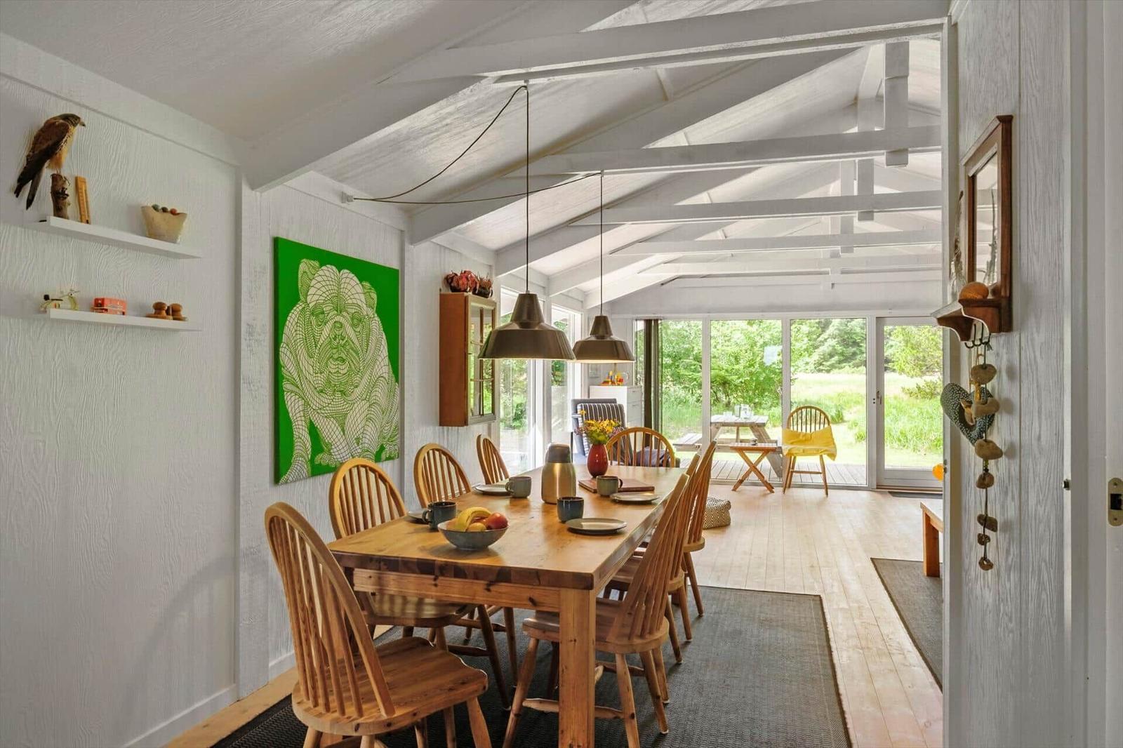 Essbereich mit Holztisch, Stühlen und grünem Wandbild. Durchgang zur Terrasse mit Gartenblick.