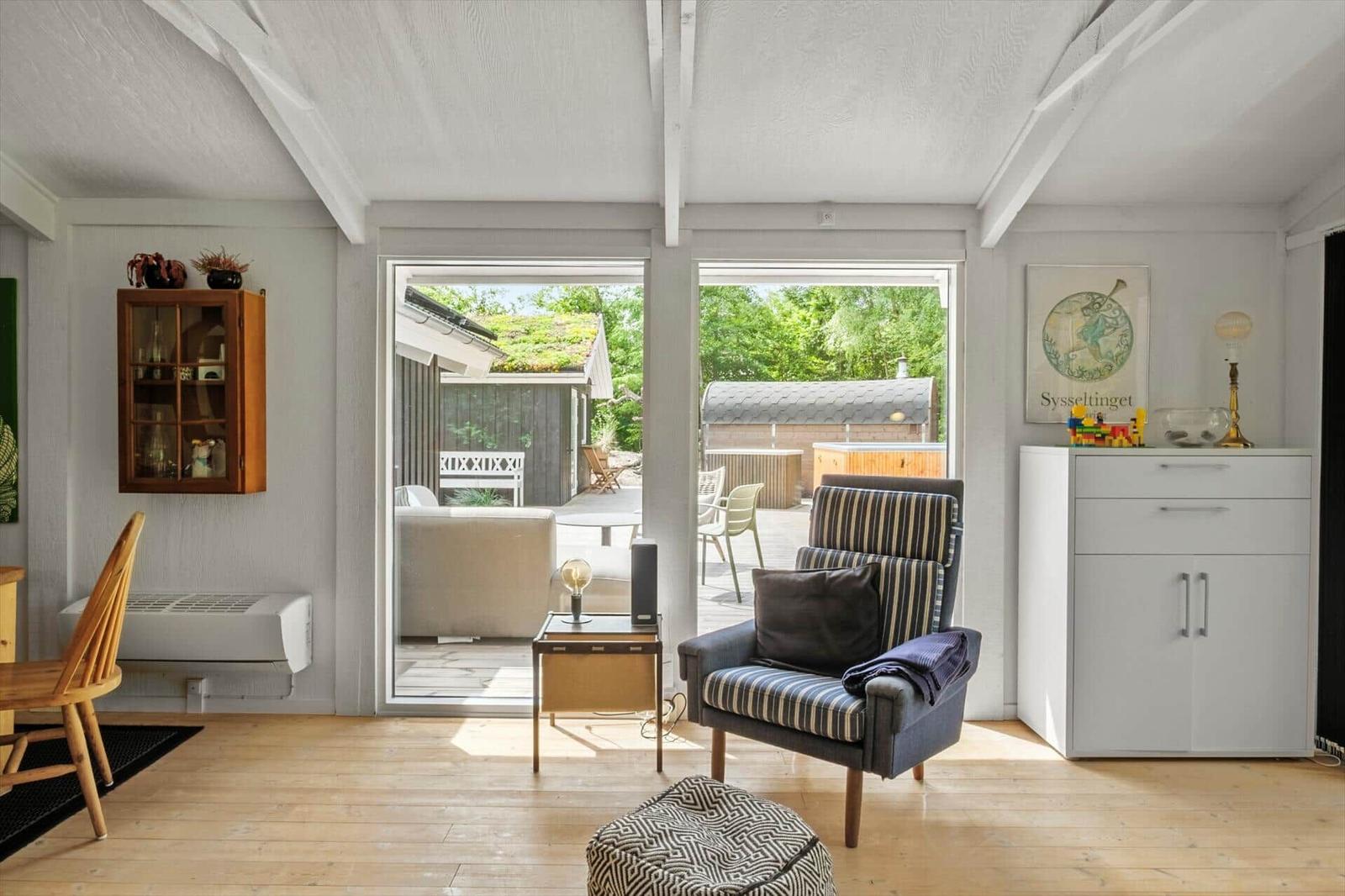 Wohnraum mit Sessel, Tisch und Blick auf Terrasse.