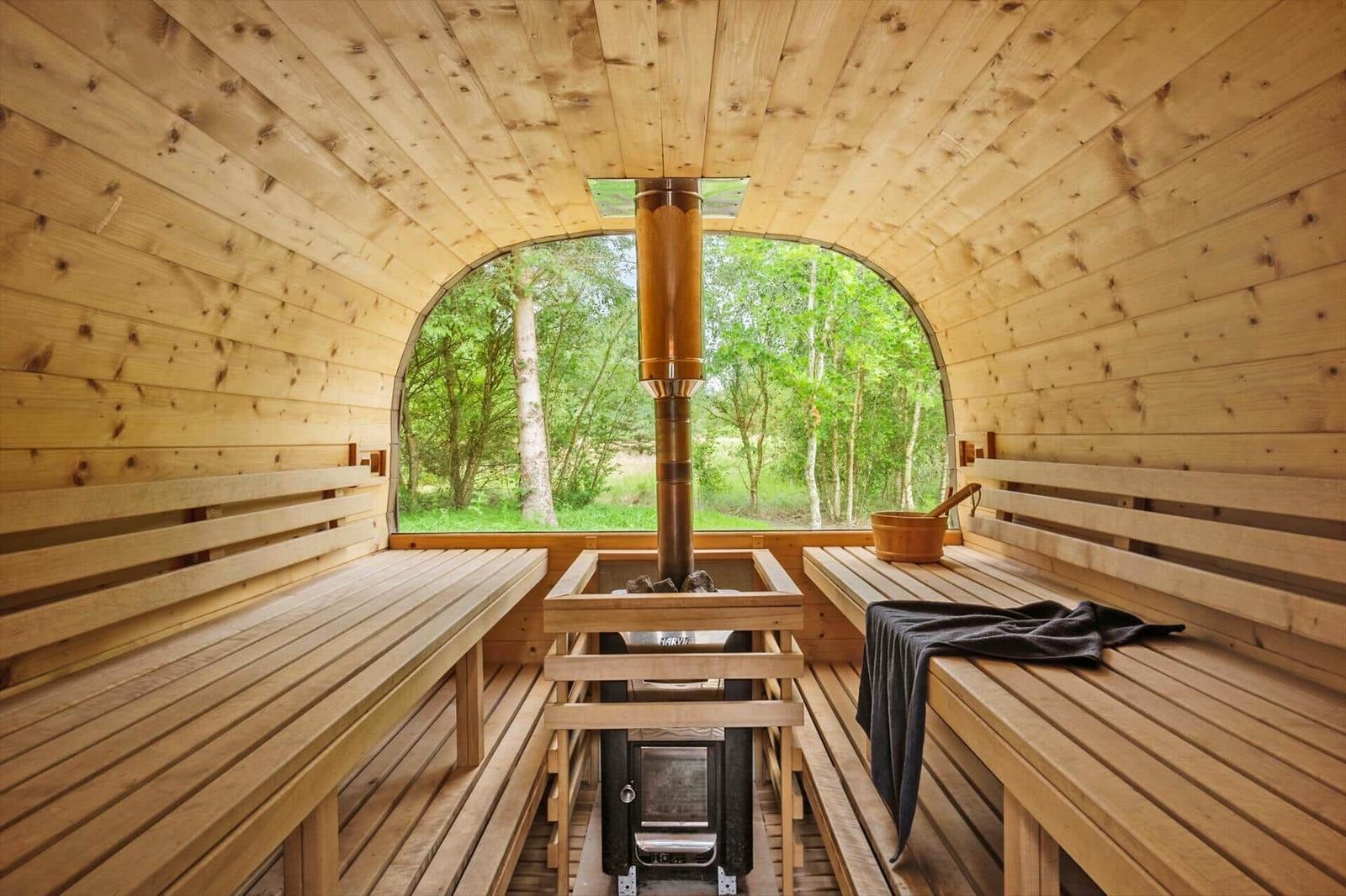 Sauna mit Holzbank, Holzdecke und großem Fenster mit Blick auf Wald.