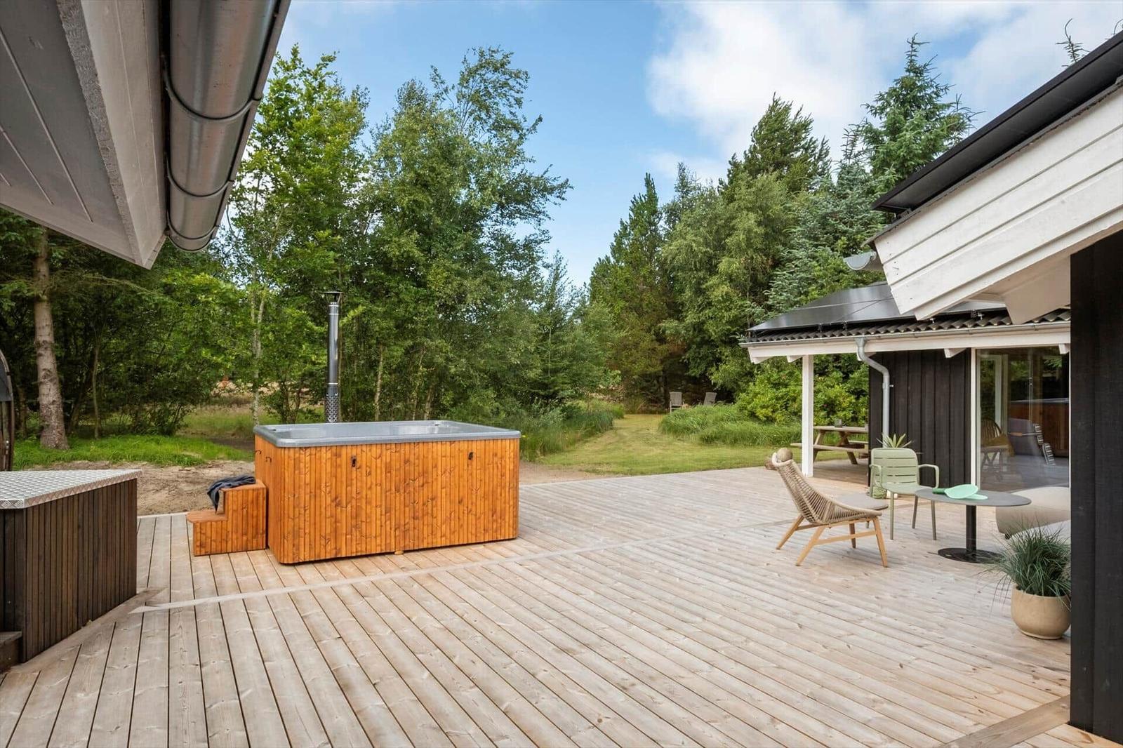 Holzterrasse mit Whirlpool, Sitzgelegenheiten und Blick in den Wald.
