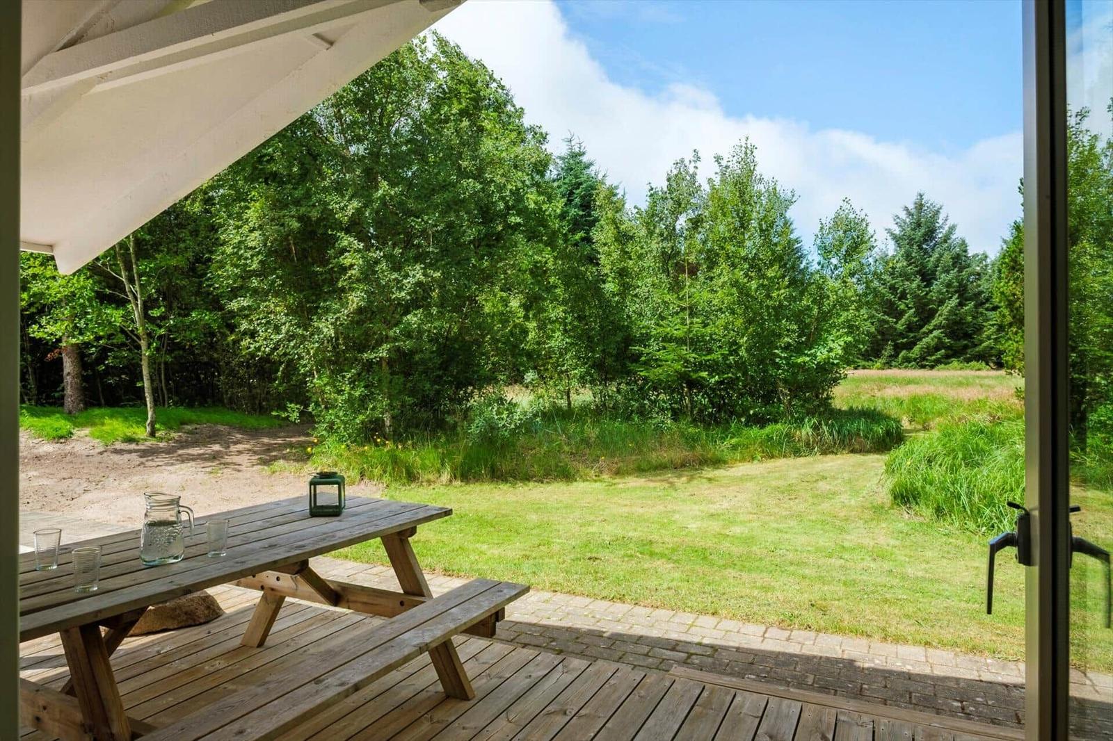 Terrasse mit Holztisch und Blick auf grüne Wiese und Wald.