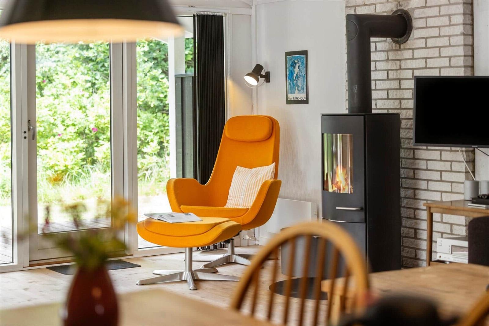 Ein Raum mit orangefarbenem Sessel, Kamin und Blick auf Garten.