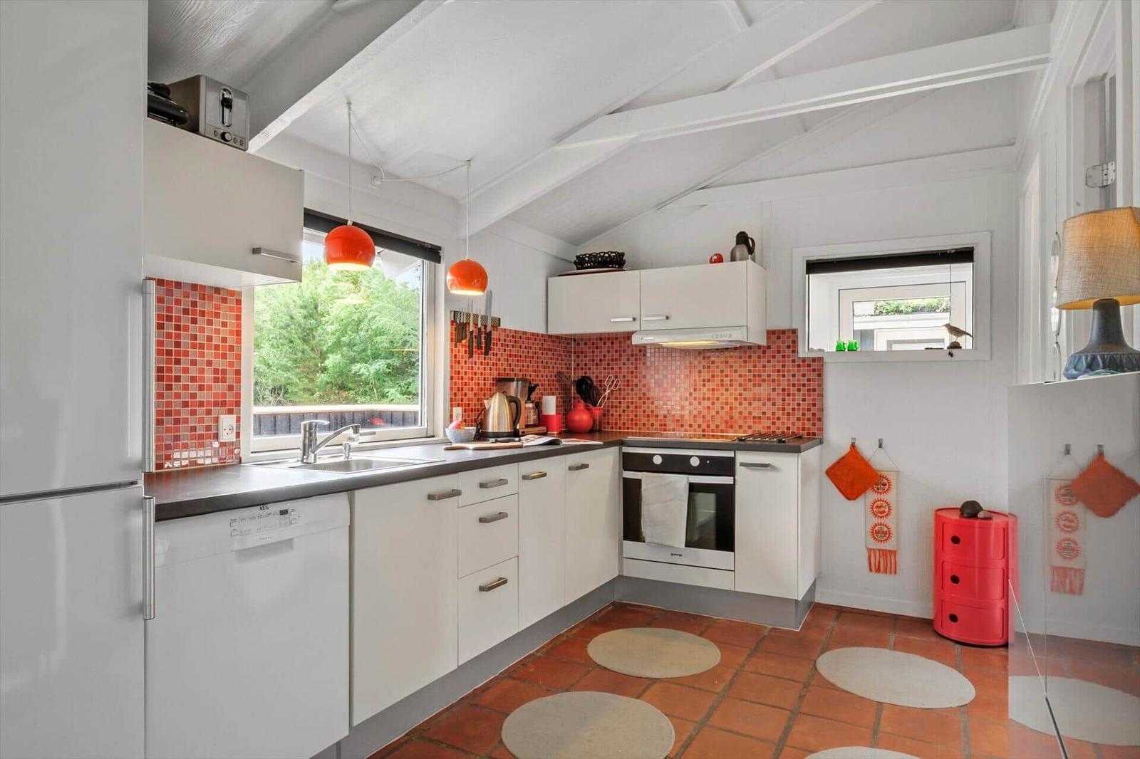 Küche mit weißen Schränken, roter Mosaikwand und Terrakottaboden