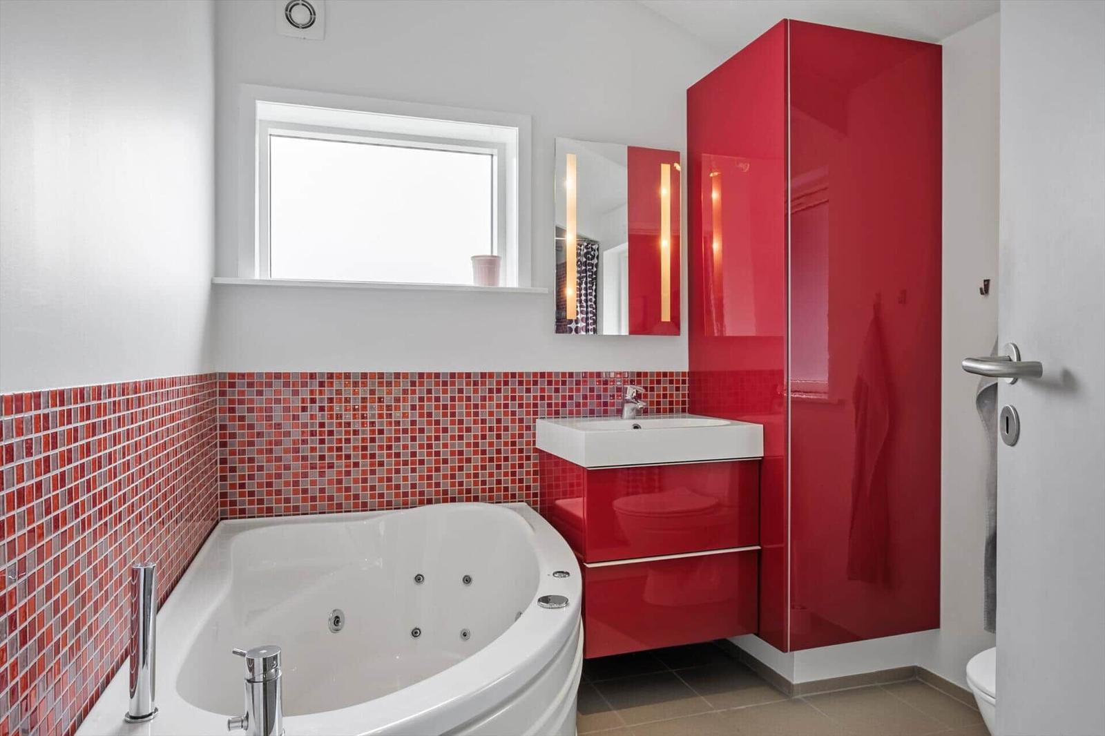 Badezimmer mit Whirlpool, rotem Schrank und Mosaikwand.