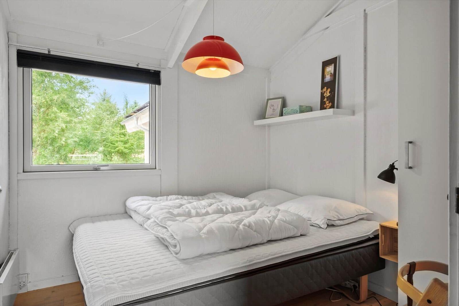 Schlafzimmer mit Bett, Fenster und roter Deckenlampe.