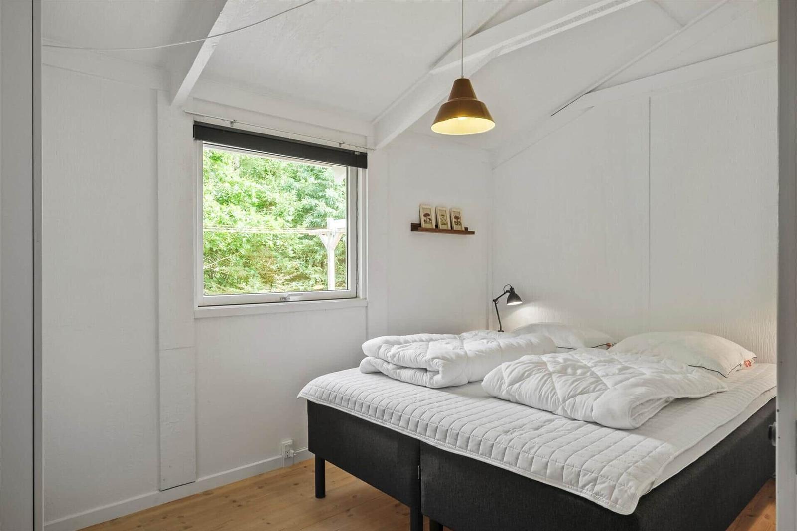 Schlafzimmer mit Doppelbett, Fenster und Deckenleuchte.