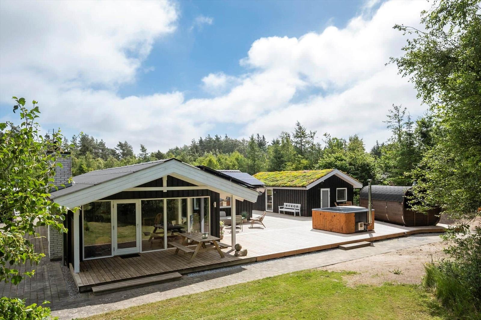 Moderne Holzhütte mit Terrasse, Whirlpool und Sauna im Wald.