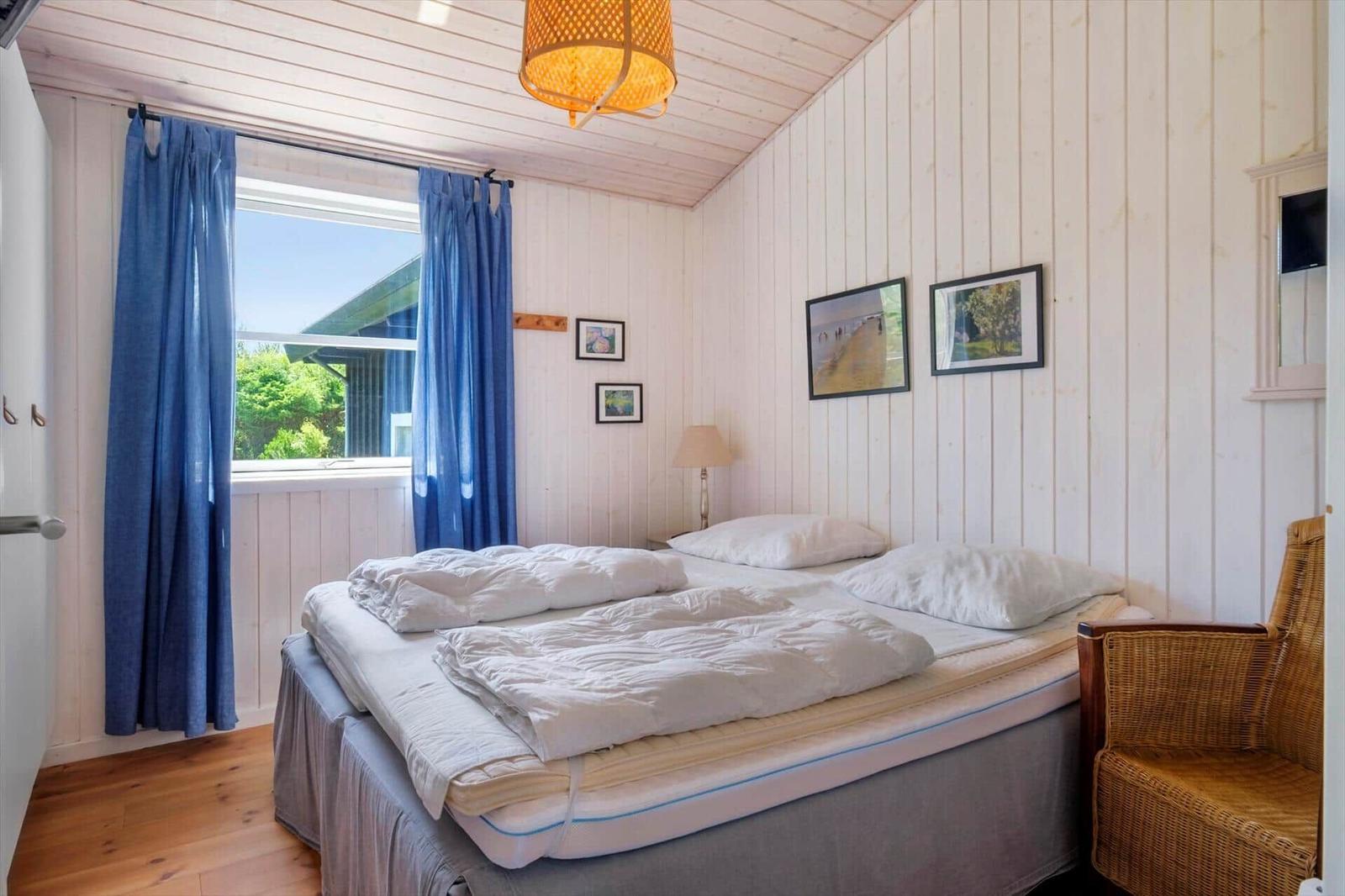 Schlafzimmer mit Bett, blauen Vorhängen und Wandbildern. Holzfußboden und weiße Wände.