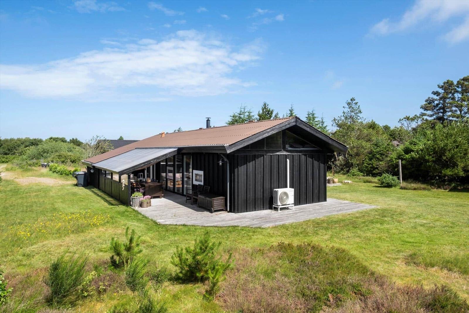 Schwarzes Holzhaus mit Terrasse und Garten. Modernes Design mit großem Fensterbereich.