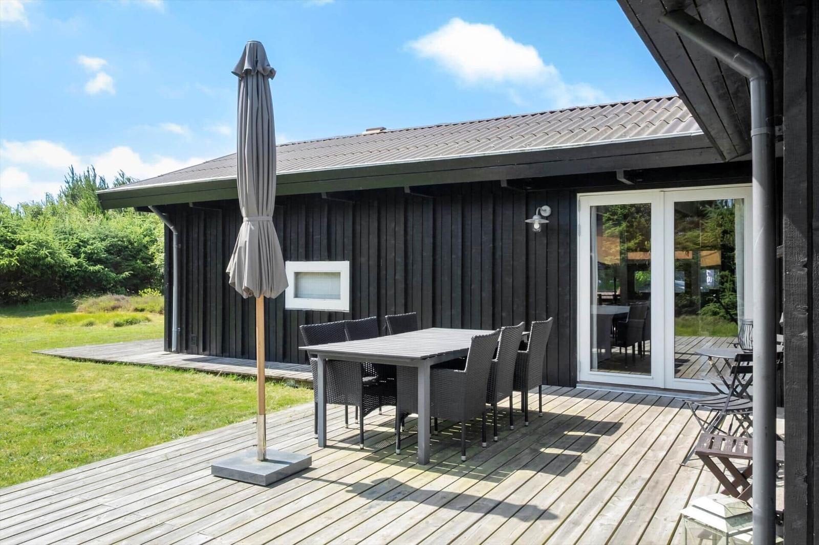 Terrasse mit Tisch, Stühlen und geschlossenem Sonnenschirm vor einem Holzhaus.
