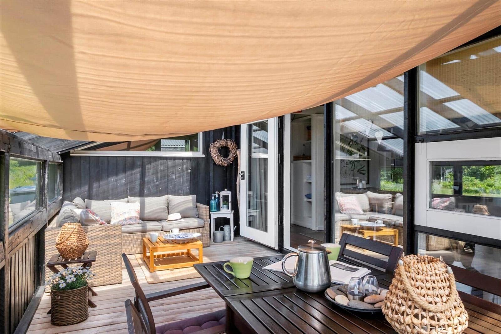 Terrasse mit Sitzgruppe, Tisch und Sonnensegel. Durchgehendes Glas verbindet Außen- und Innenbereich.