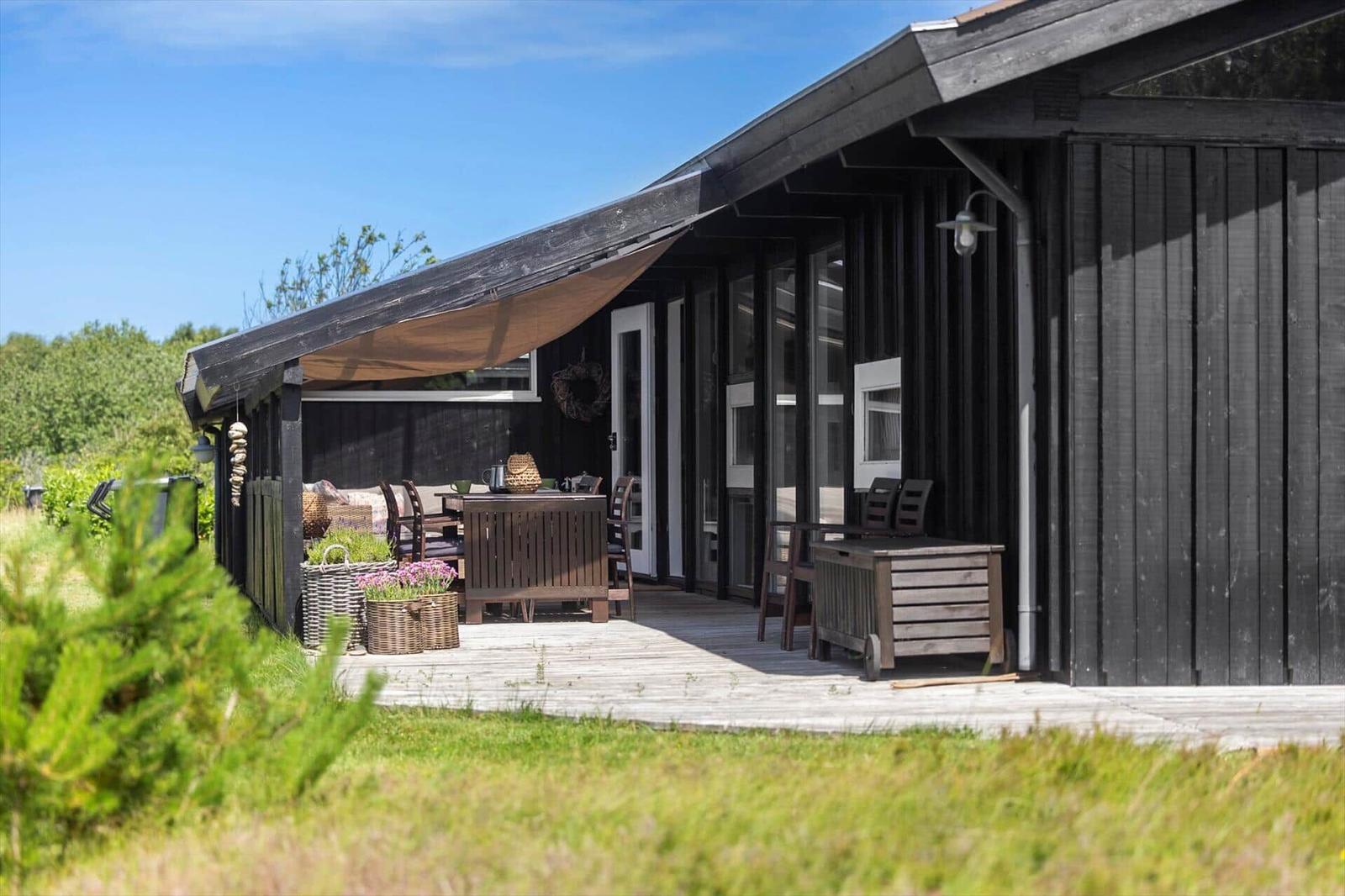 Terrasse mit Tisch, Stühlen und Sonnensegel vor einem Holzhaus.